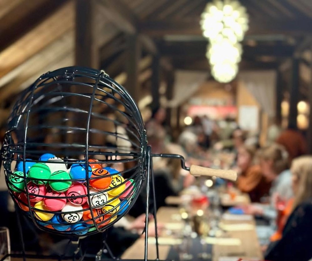 Bilde av mennesker som sitter langs et langbord i langhuset og spiller bingo